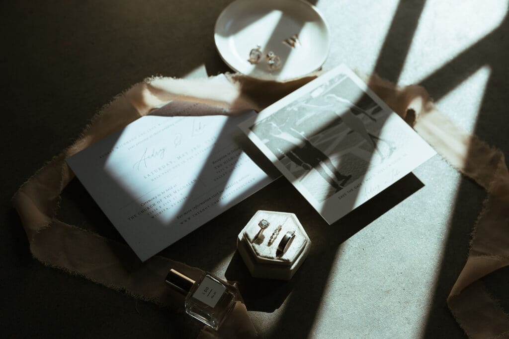 Flat lay of wedding details including rings, earrings, invites and perfume.