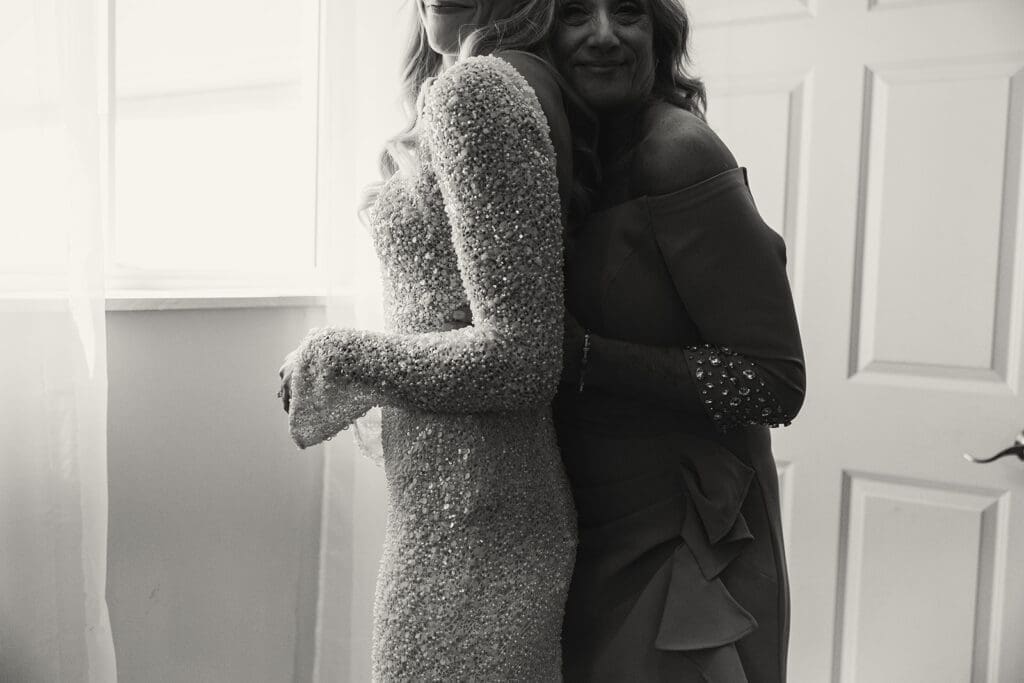 Mother of the bride embraces bride in her wedding dress.